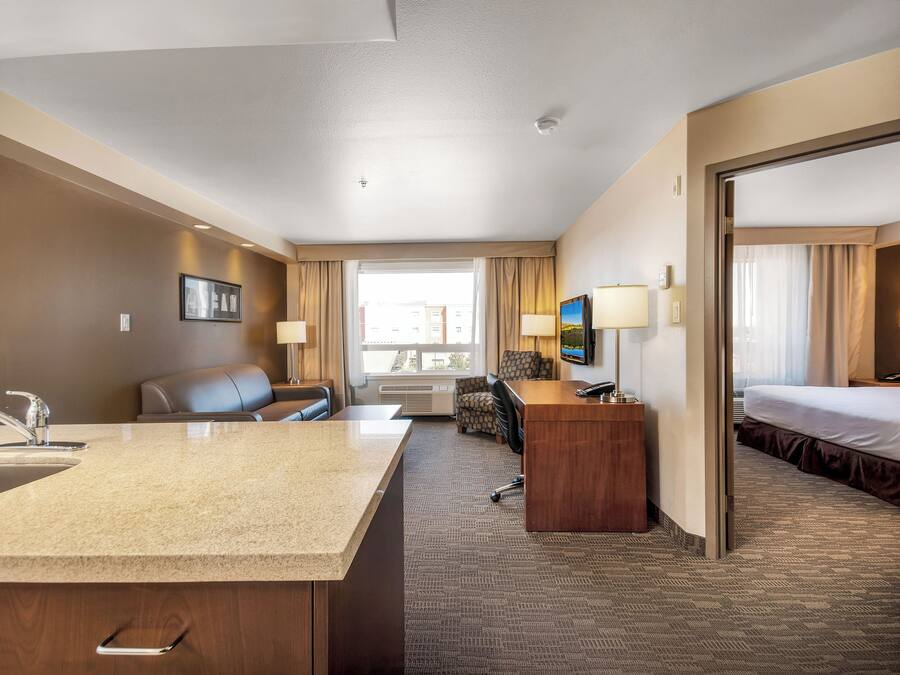 Quarto de hotel com cozinha compacta, cama, escrivaninha e área de estar.