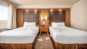 Habitación de hotel con dos camas, una mesita de noche con lámpara y una ventana con cortinas.