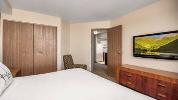 Quarto de hotel com cama, televisão na parede, guarda-roupa de madeira e uma cadeira.