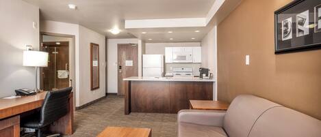 A hotel room with a wooden desk, black office chair, beige sofa, and a small wooden table.