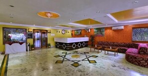 Welcome to our hotel lobby, featuring a geometric patterned floor, a reception desk with a clock, and comfortable seating area with a sofa and table.