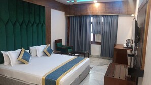 Habitación de hotel con una cama grande, un escritorio, una silla, un televisor y una ventana con cortinas.