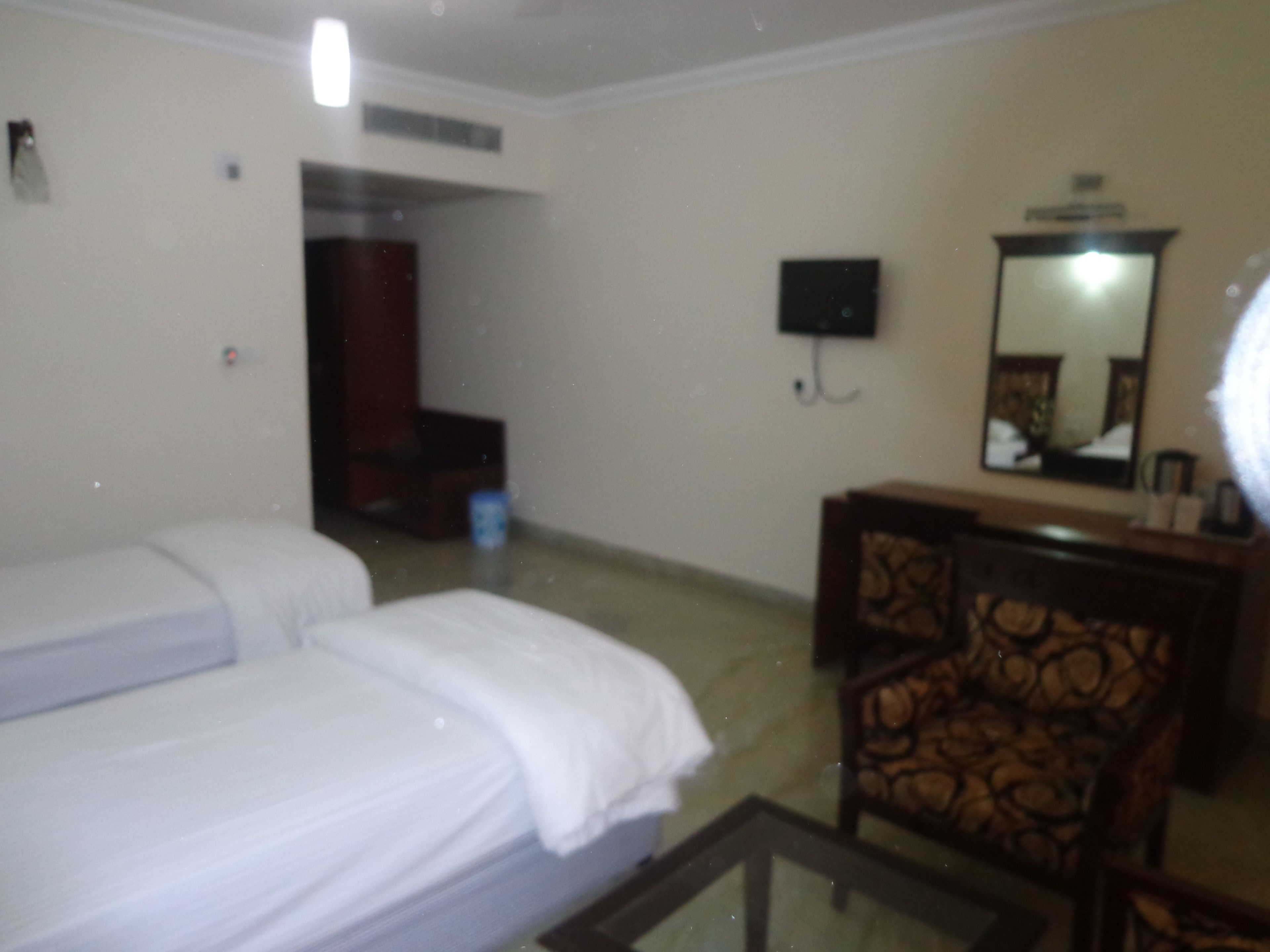 A hotel room with two beds, a desk, a chair, a mirror, and a television.