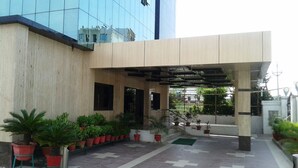 Un edificio moderno con un área de entrada cubierta, plantas en macetas y una escalera que conduce a un nivel superior.