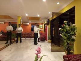 Vestíbulo de hotel con recepción, asientos y una planta en maceta grande.