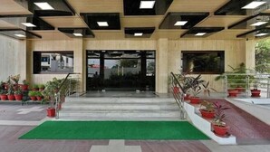 Entrada de un edificio con alfombra verde, plantas en macetas y una escalera que conduce a la entrada.