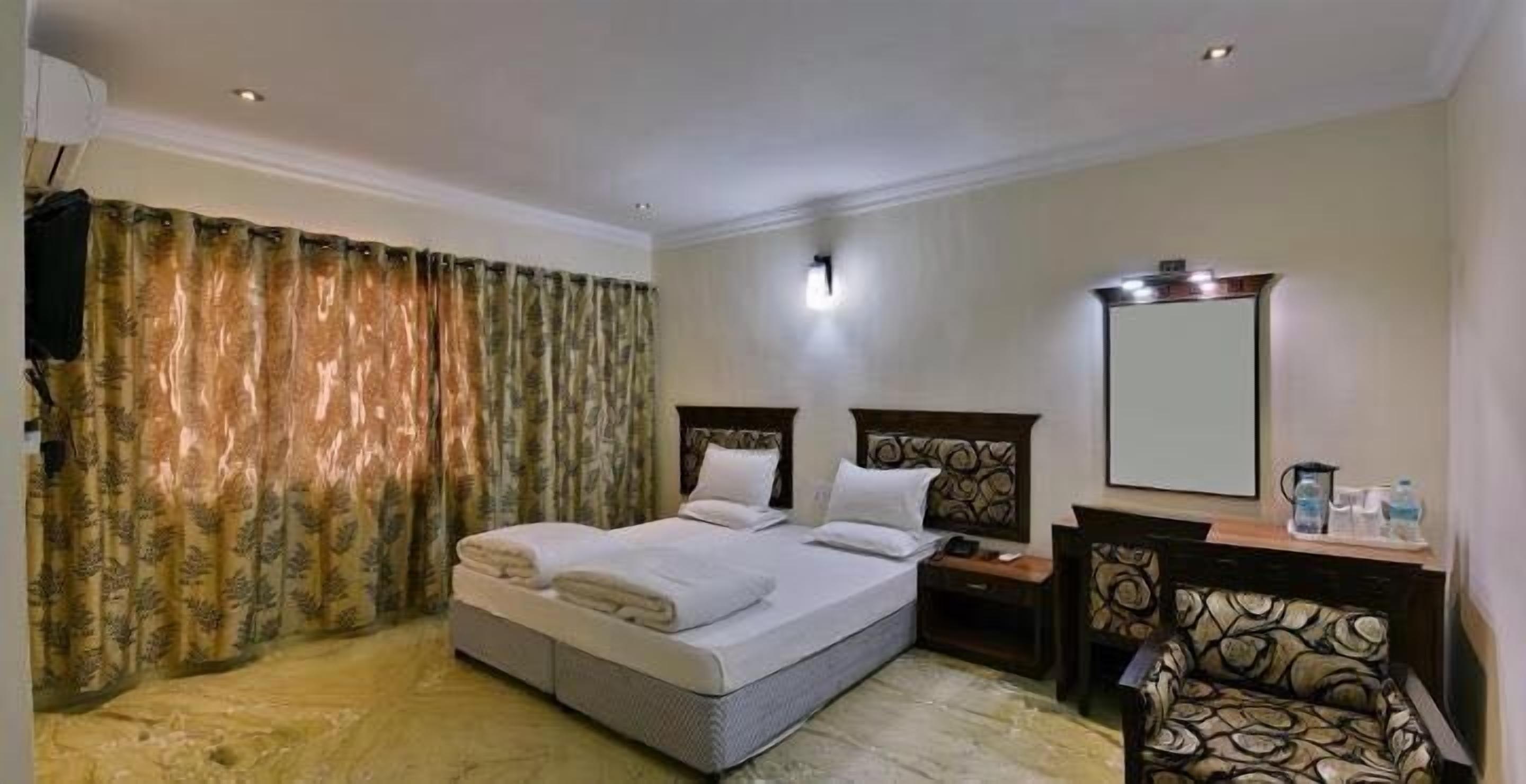 A hotel room with a bed, a nightstand, a chair, a mirror, and curtains.