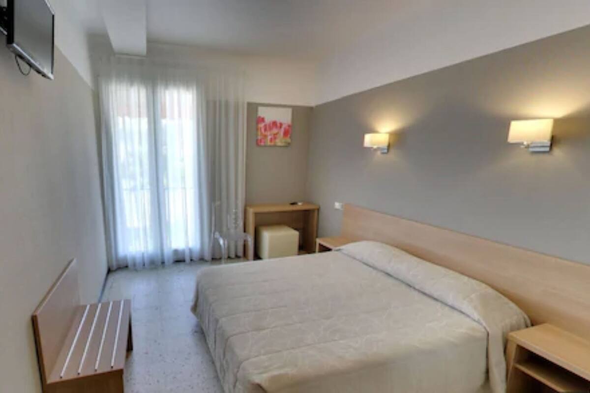 A hotel room with a bed, bedside tables, a desk, a chair, and a window with curtains.