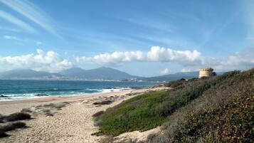 A coastal landscape with a sandy beach, a tower, and mountains in the background.