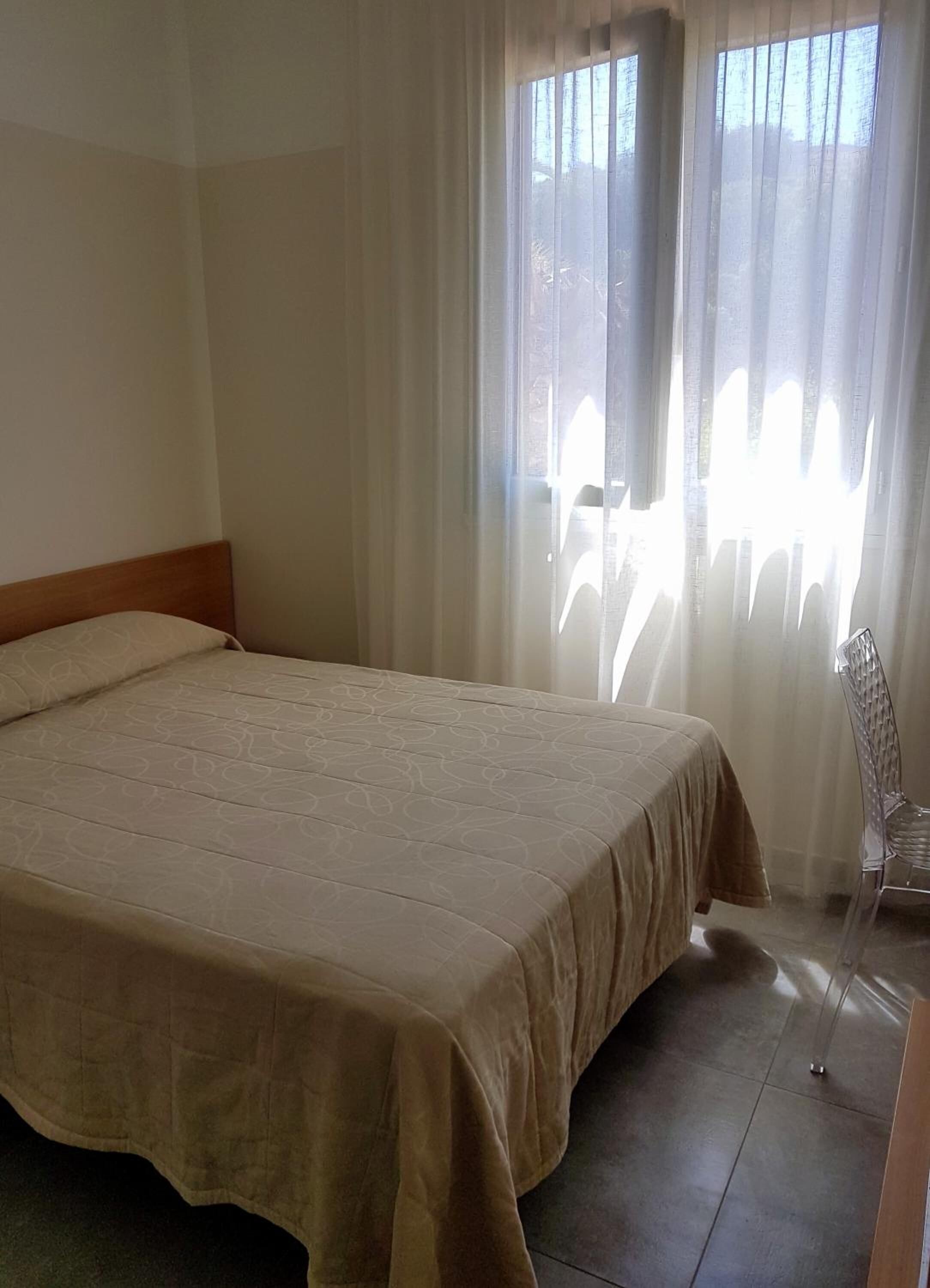 A hotel room with a large bed, a chair, and a window with sheer curtains.
