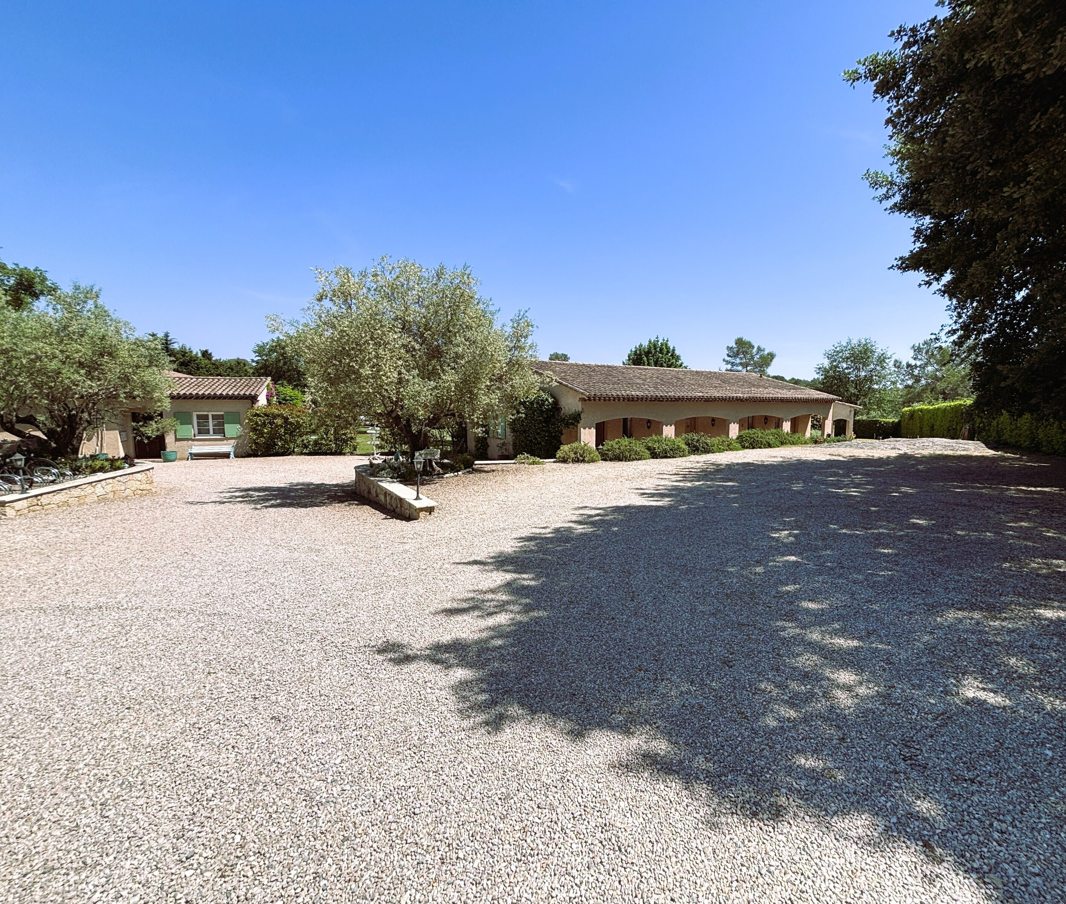 A building with a gravel driveway, a bench, and a tree in the foreground.