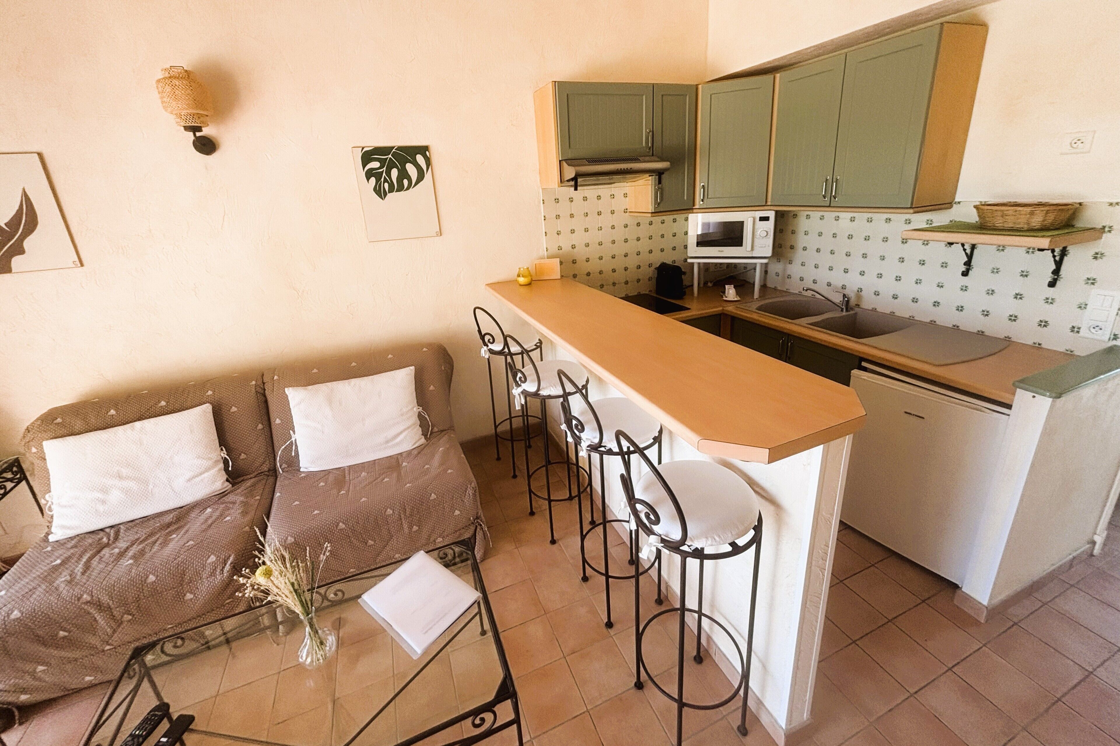 A compact kitchen with a bar area, a dining table with chairs, and a sofa with cushions.