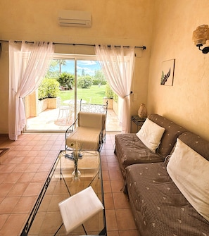 A living room with a sofa, a chair, a glass coffee table, and a view of a garden through a sliding door. - La Résidence du Moulin (Tourrettes-sur-Loup)