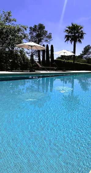 A clear swimming pool with a tiled edge, surrounded by trees and umbrellas. - La Résidence du Moulin (Tourrettes-sur-Loup)