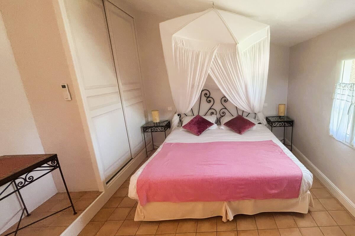 A bedroom with a bed, a canopy, two nightstands, a window, and a door.