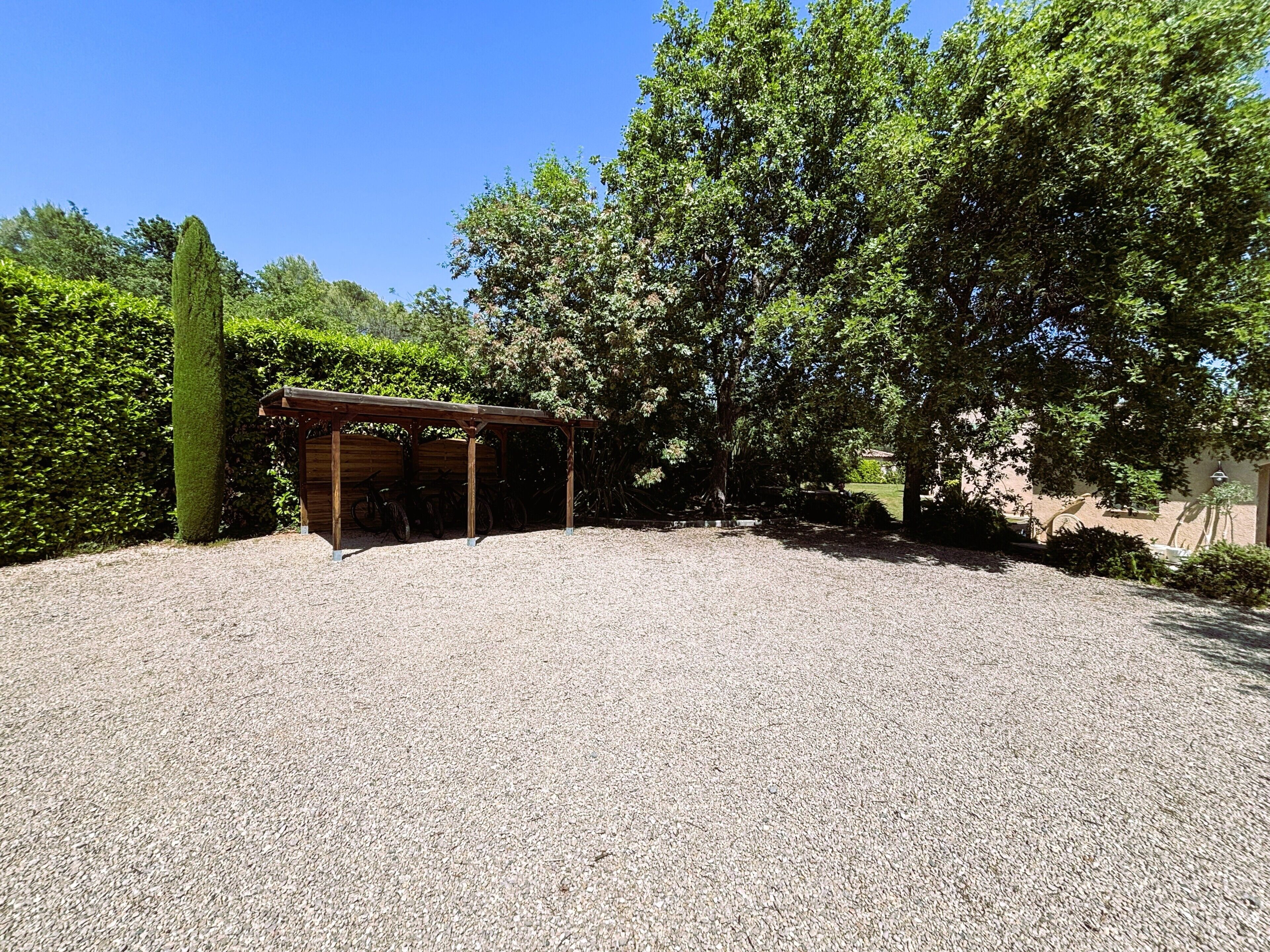 A gravel-covered parking area with a wooden shelter and bicycles.