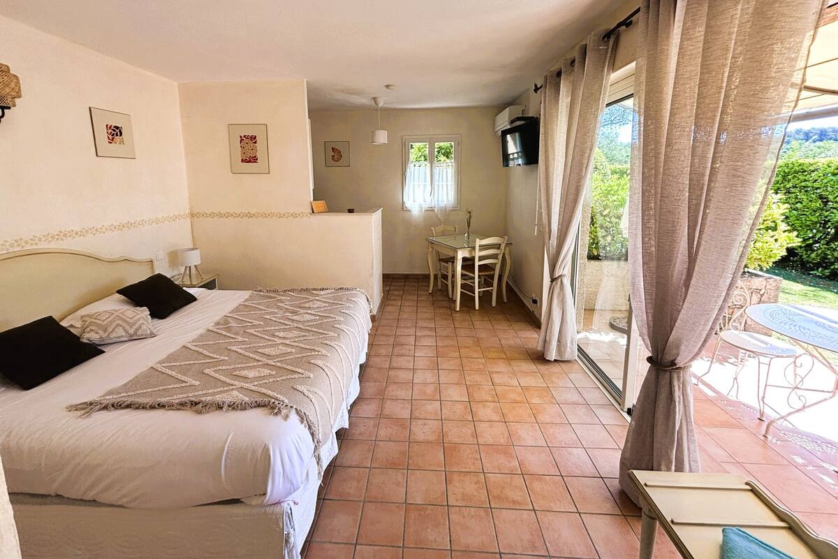 A bedroom with a bed, a small table, a chair, and a window with curtains.