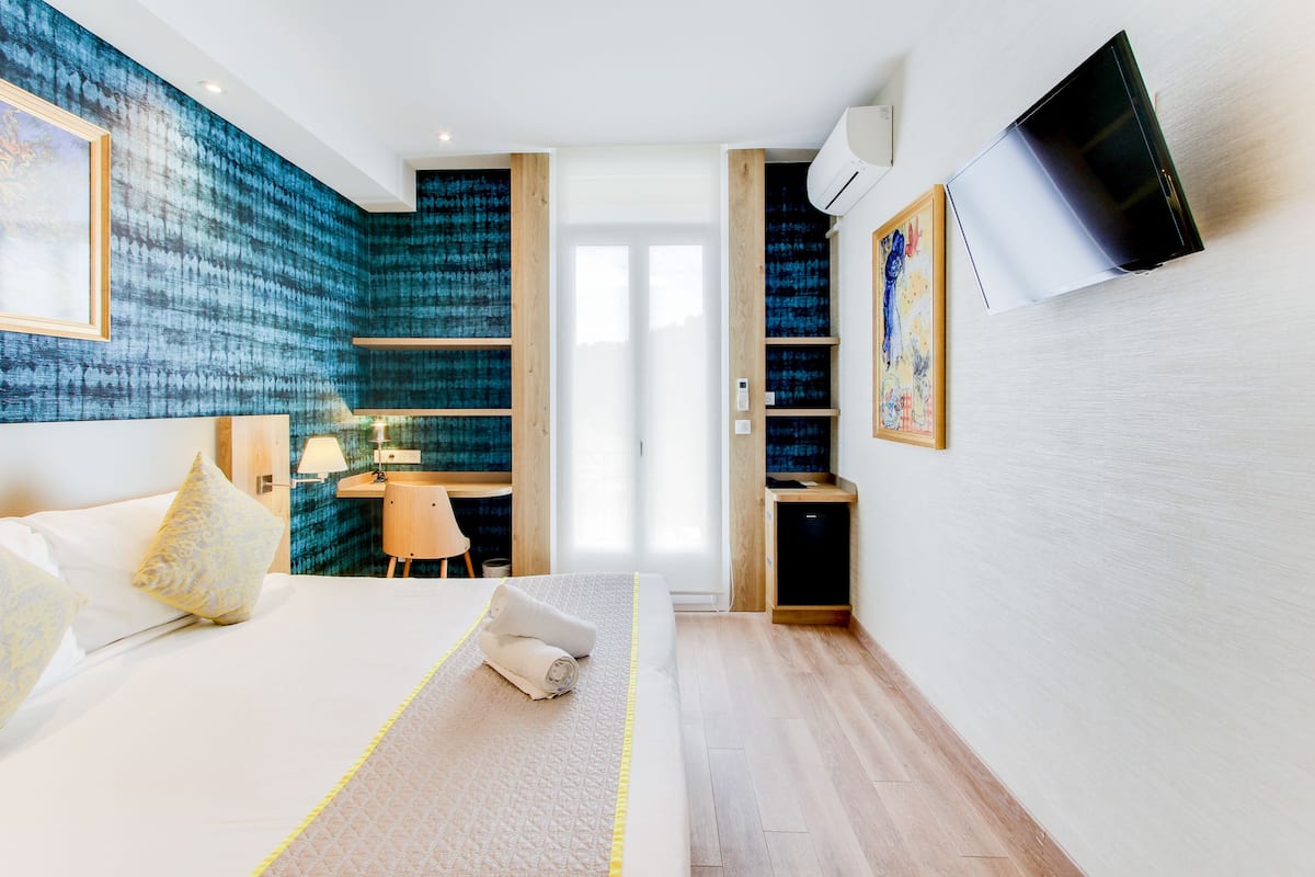 A modern hotel room with a large bed, a desk, and a TV mounted on the wall.