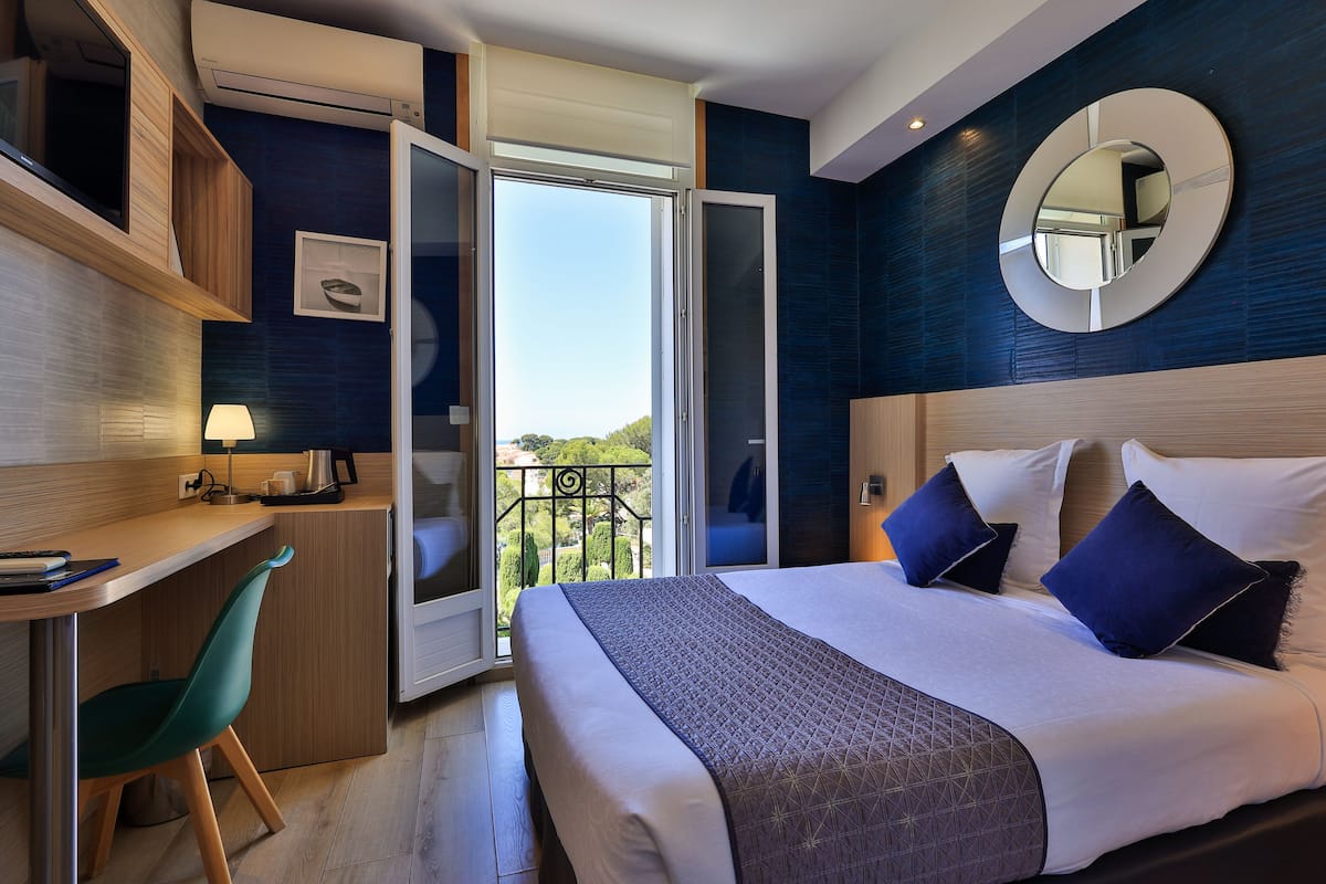 A modern hotel room with a bed, a desk, a chair, and a balcony with a view.