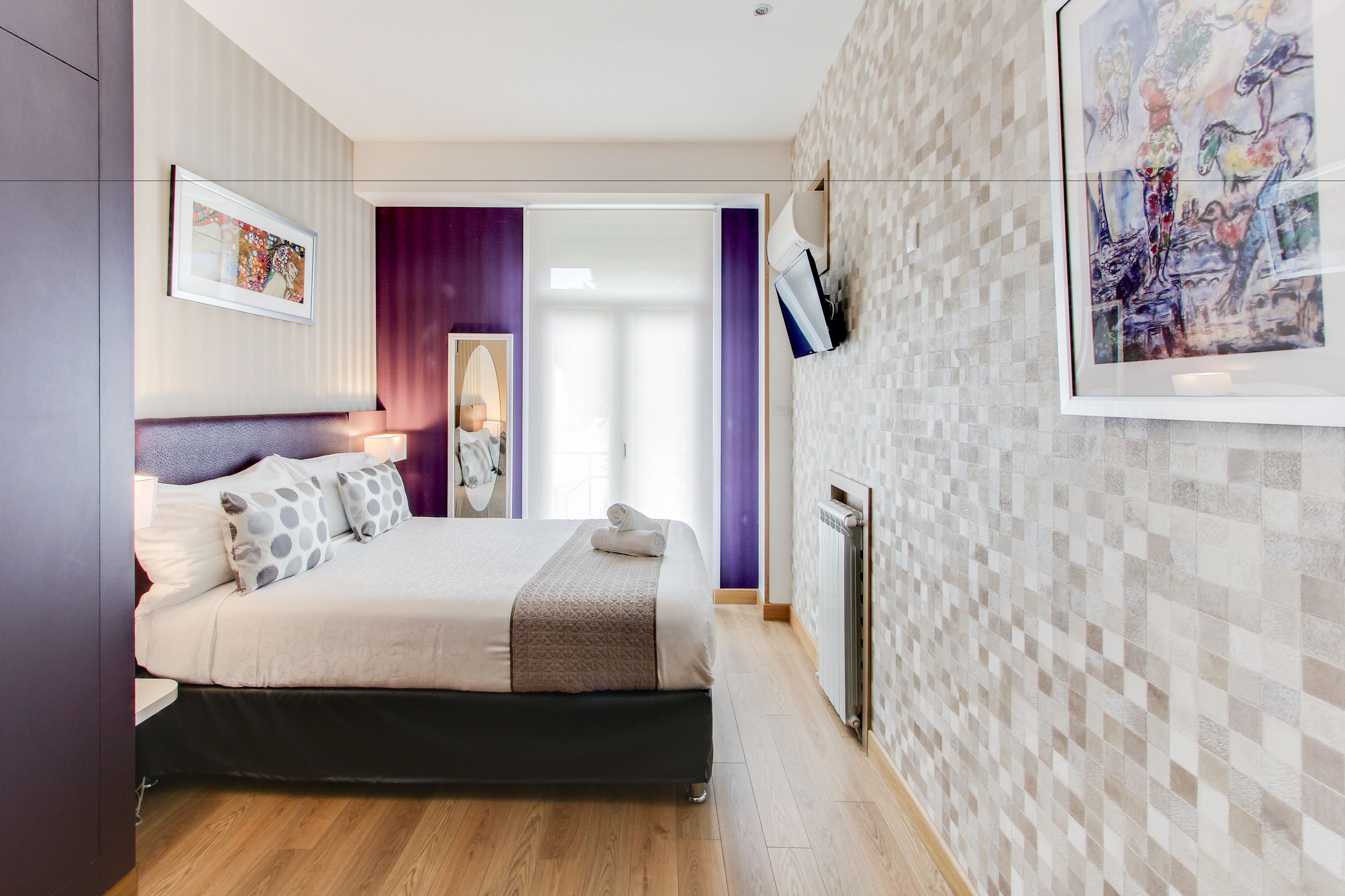 Um quarto moderno com uma cama, uma mesinha de cabeceira, um aquecedor fixado na parede e uma obra de arte emoldurada.