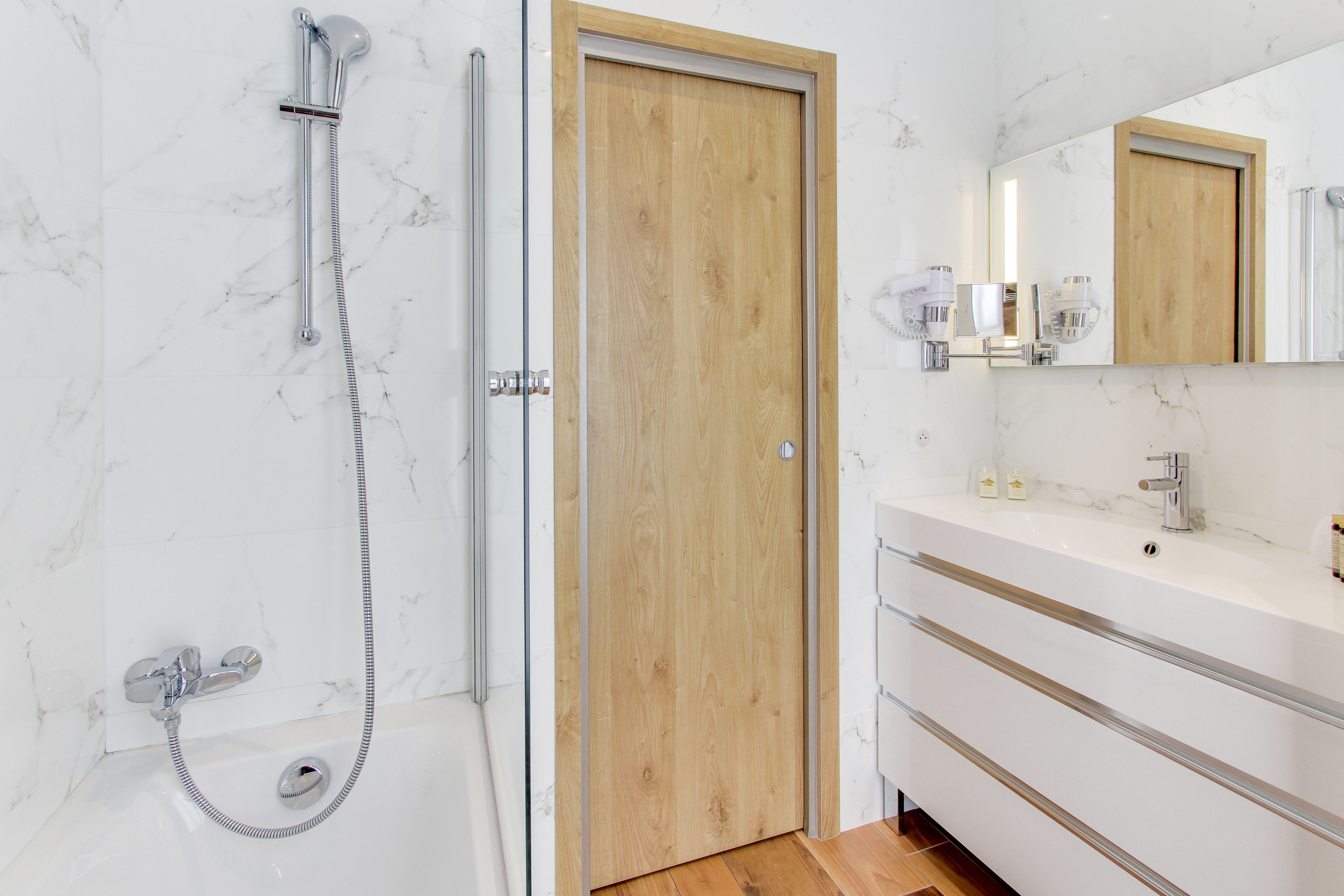 Un bagno moderno con doccia, una porta in legno, un mobile lavabo con specchio e un lavandino.