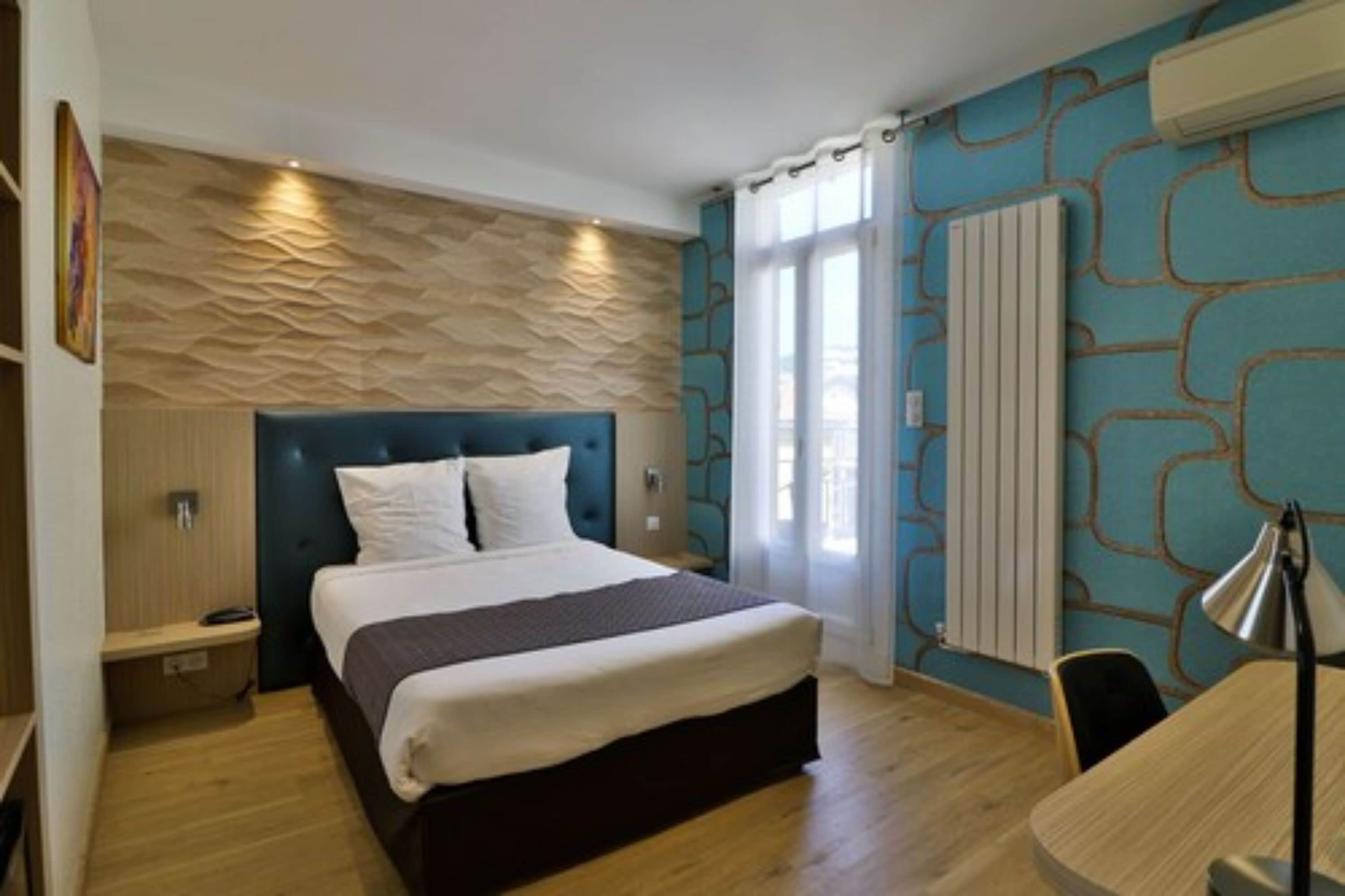 A modern hotel room with a large bed, a wooden floor, a blue accent wall, and a radiator.