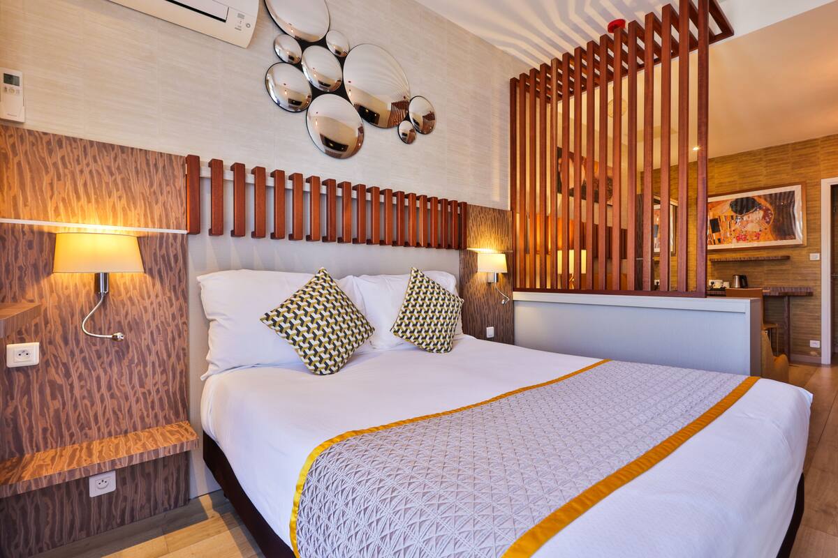 A modern hotel room with a large bed, patterned pillows, a wooden headboard, and wall-mounted lights.