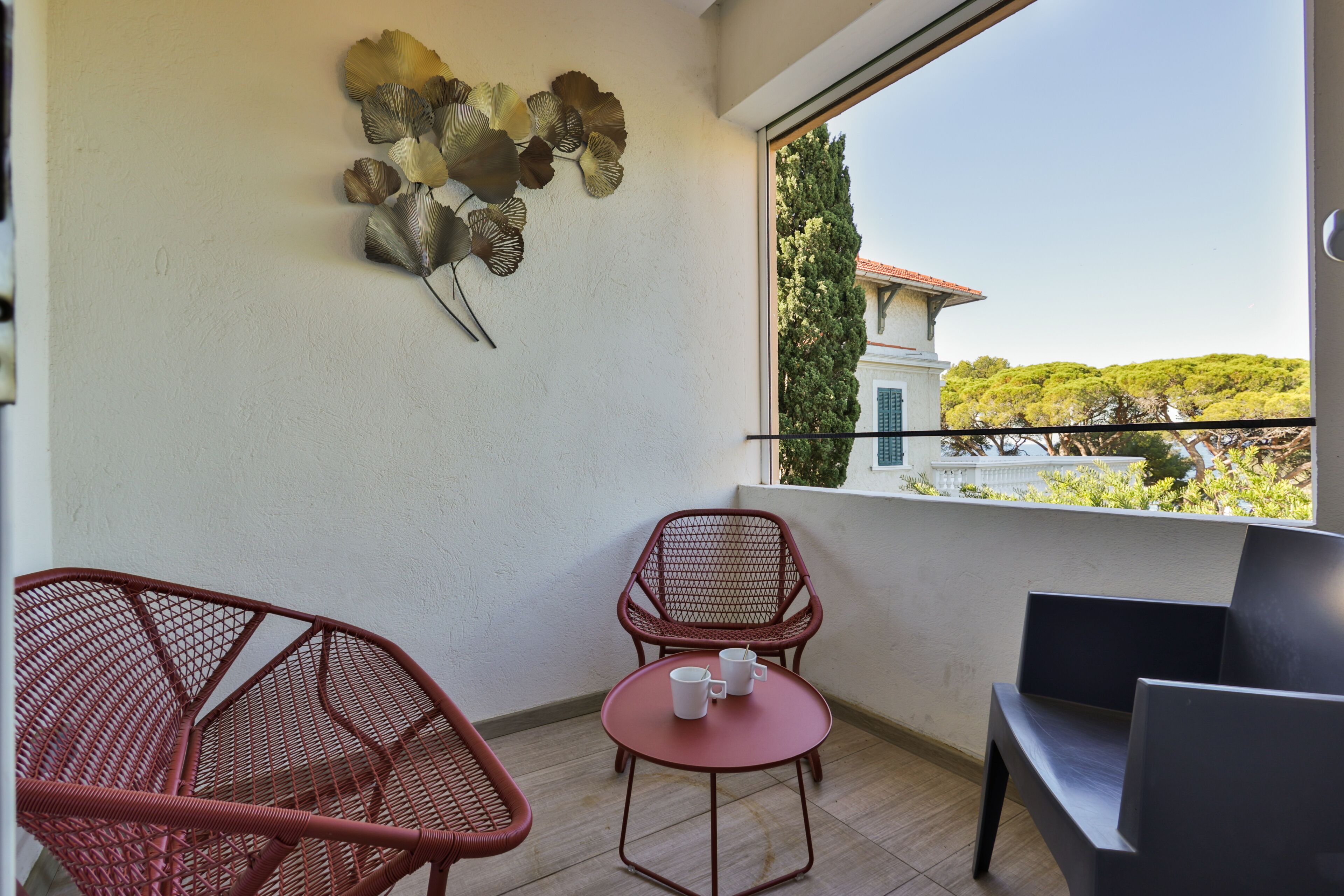 A balcony with wicker chairs, a small table, and a decorative wall piece.