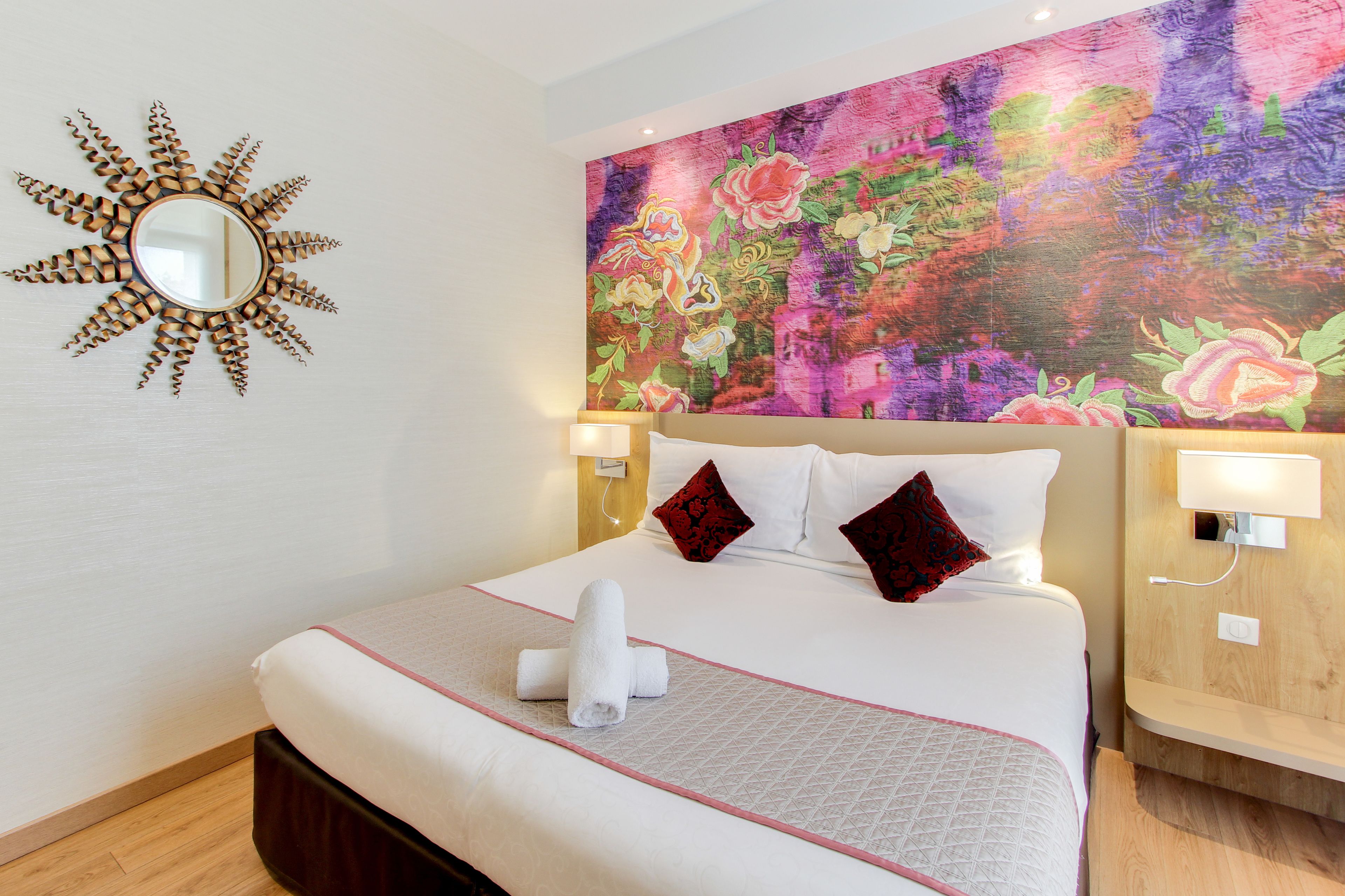 Una habitación de hotel con una cama grande, un espejo decorativo y un cuadro floral colorido en la pared.