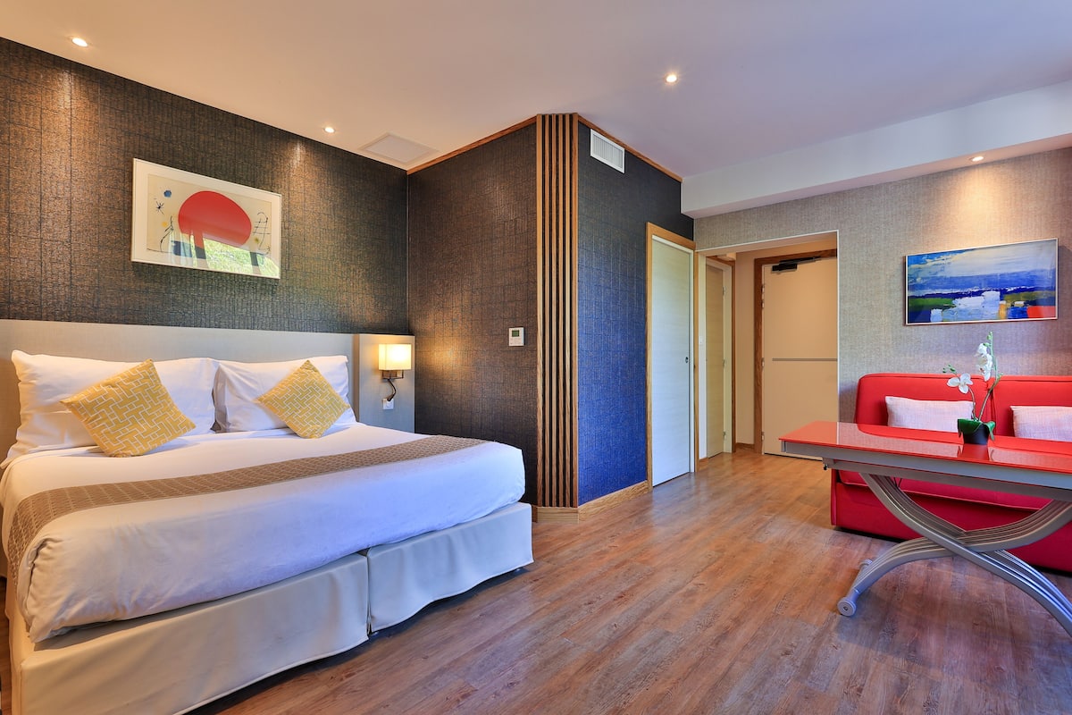 A hotel room with a large bed, a red sofa, and artwork on the walls.