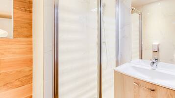 Un baño moderno con cabina de ducha de vidrio, tocador de madera y un espejo grande.