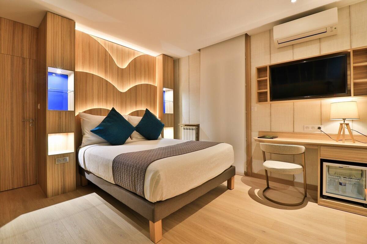 A modern bedroom with a bed, bedside tables, a desk, and a television.