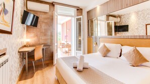Quarto de hotel com cama, secretária e televisão fixada na parede.