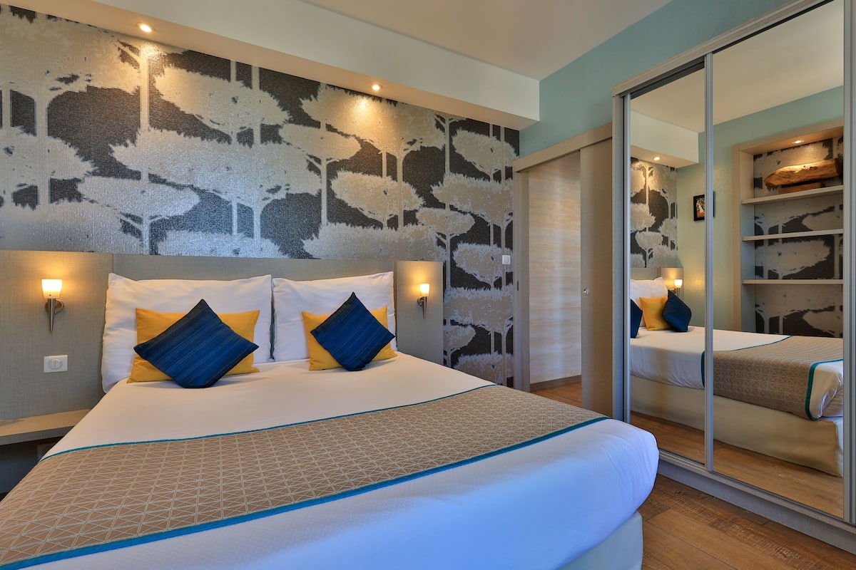 A hotel room with a large bed, a mirror, and a wall with a textured pattern.