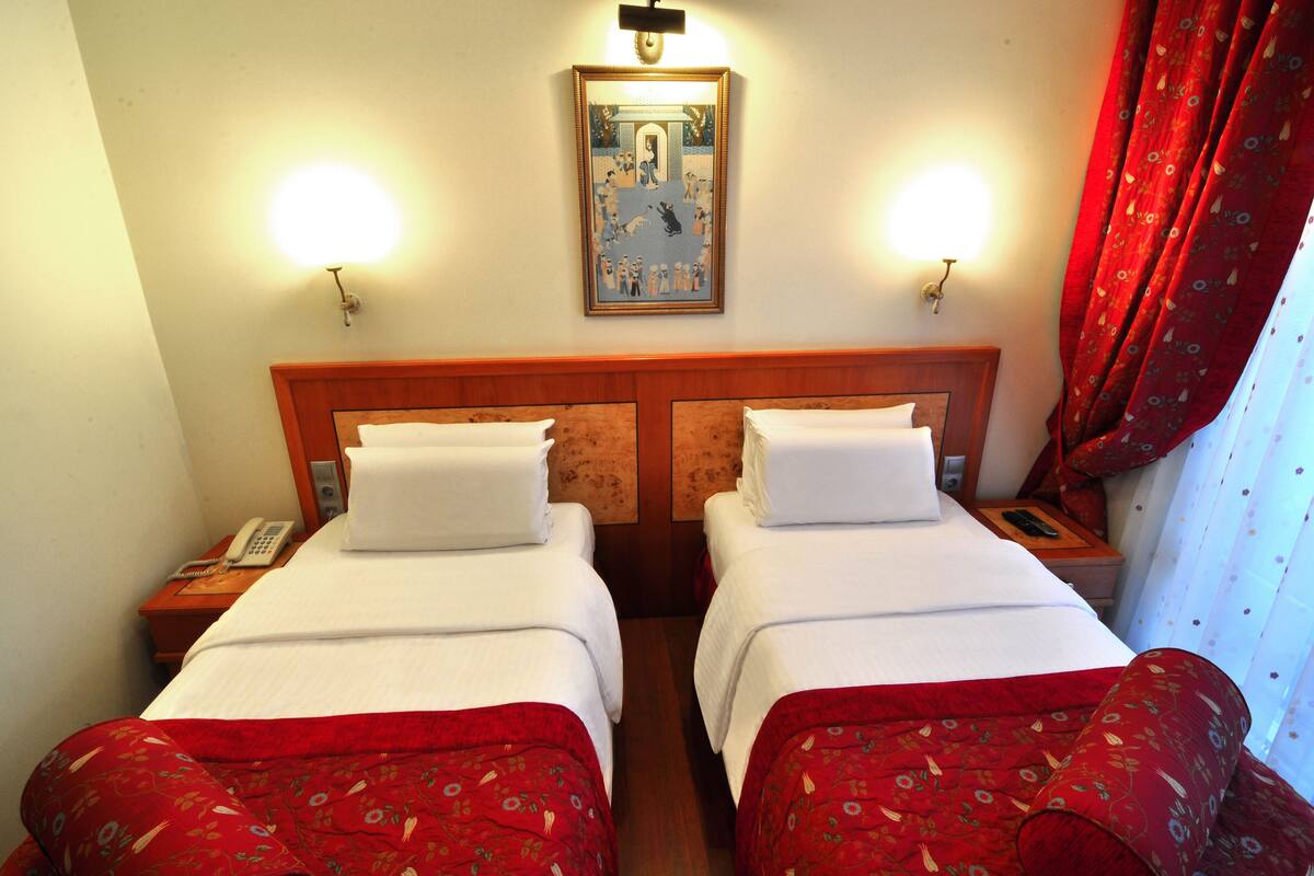 A hotel room with two single beds, a wooden headboard, a painting above the beds, and a telephone on the nightstand.