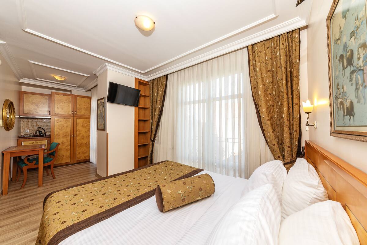 A hotel room with a bed, a desk, a chair, a television, and a painting on the wall.