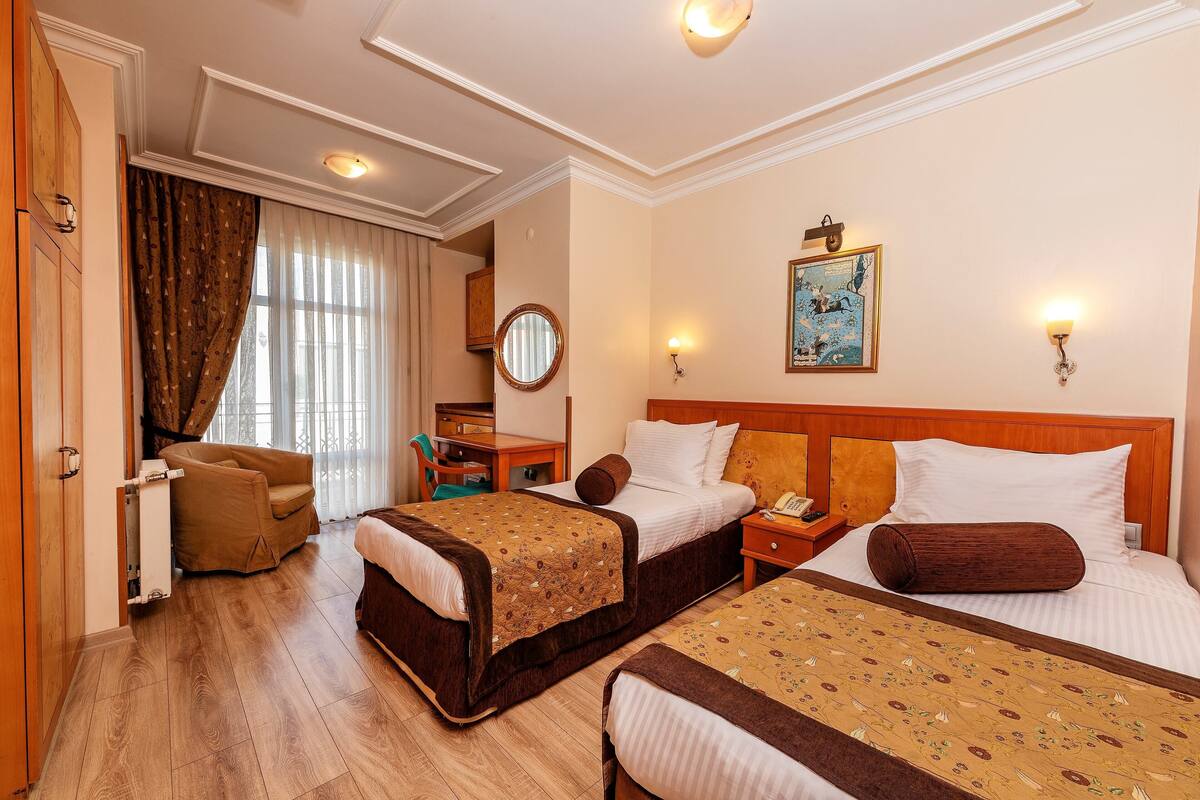 A hotel room with two beds, a desk, a chair, and a large window with curtains.