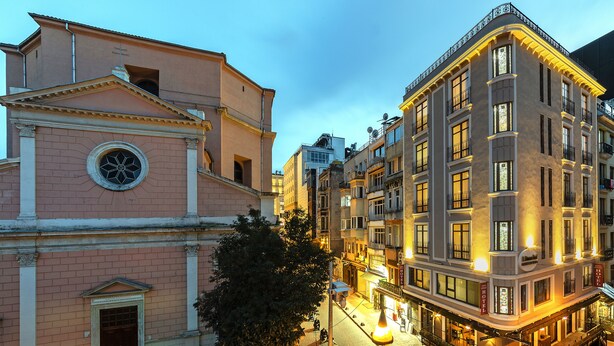 Un edificio histórico con una destacada torre de reloj, un amplio ventanal de arco y un balcón con barandilla.