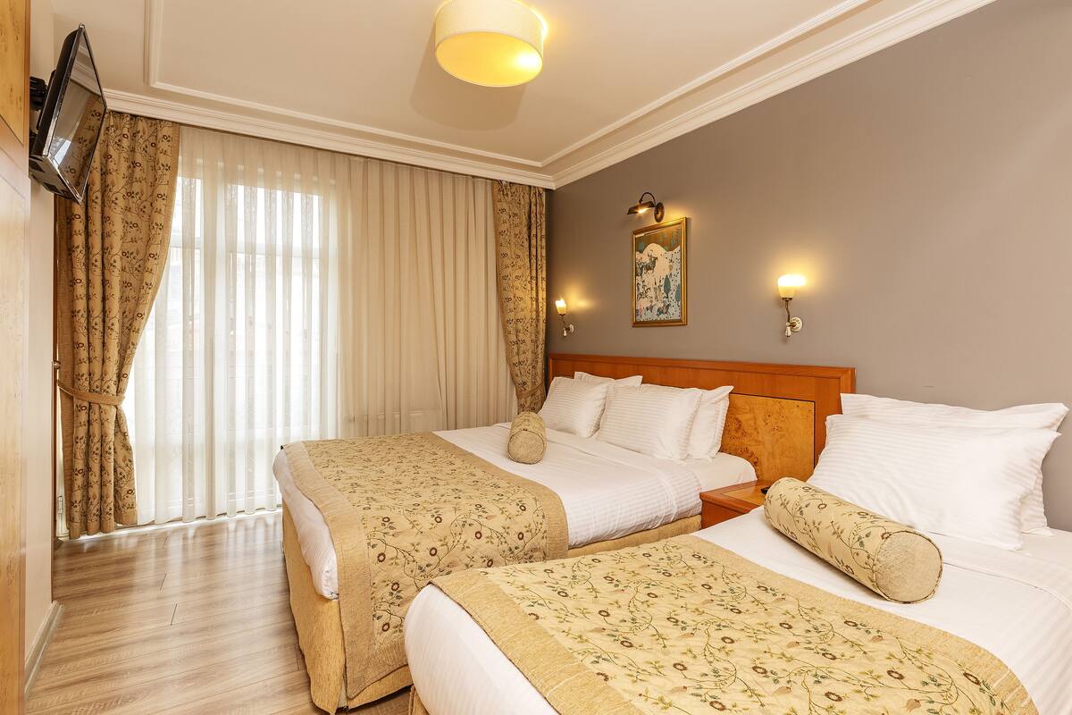 A hotel room with two beds, a TV, a painting, and a window with curtains.