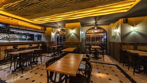 Un restaurante con mesas y sillas de madera, una zona de bar con vasos y un techo con motivos decorativos.
