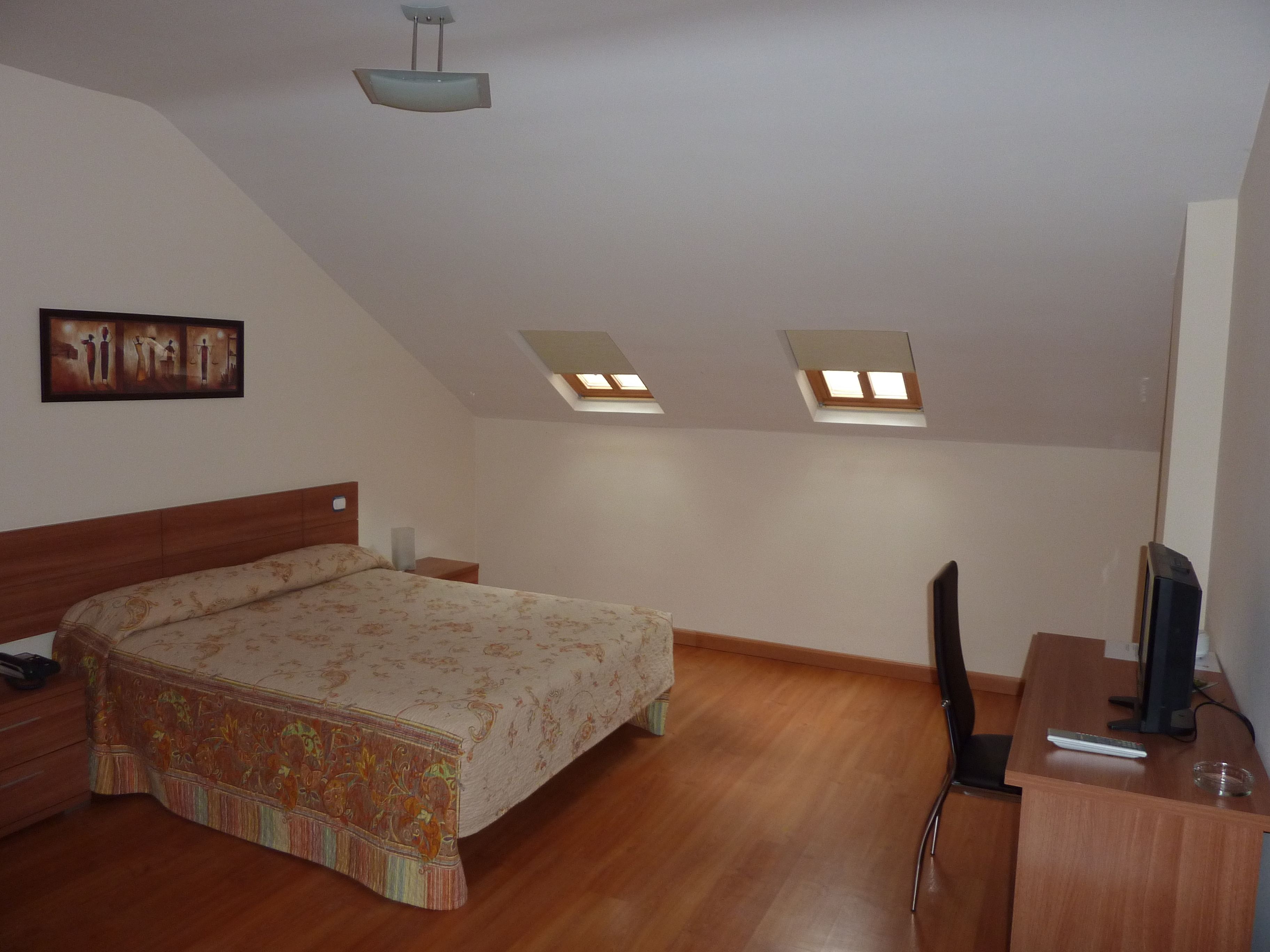 A bedroom with a bed, a desk, a chair, and two skylights.