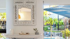 Uma mesa branca de estilo rústico com um espelho decorativo em cima, em um quarto claro com vista para a piscina e área externa.