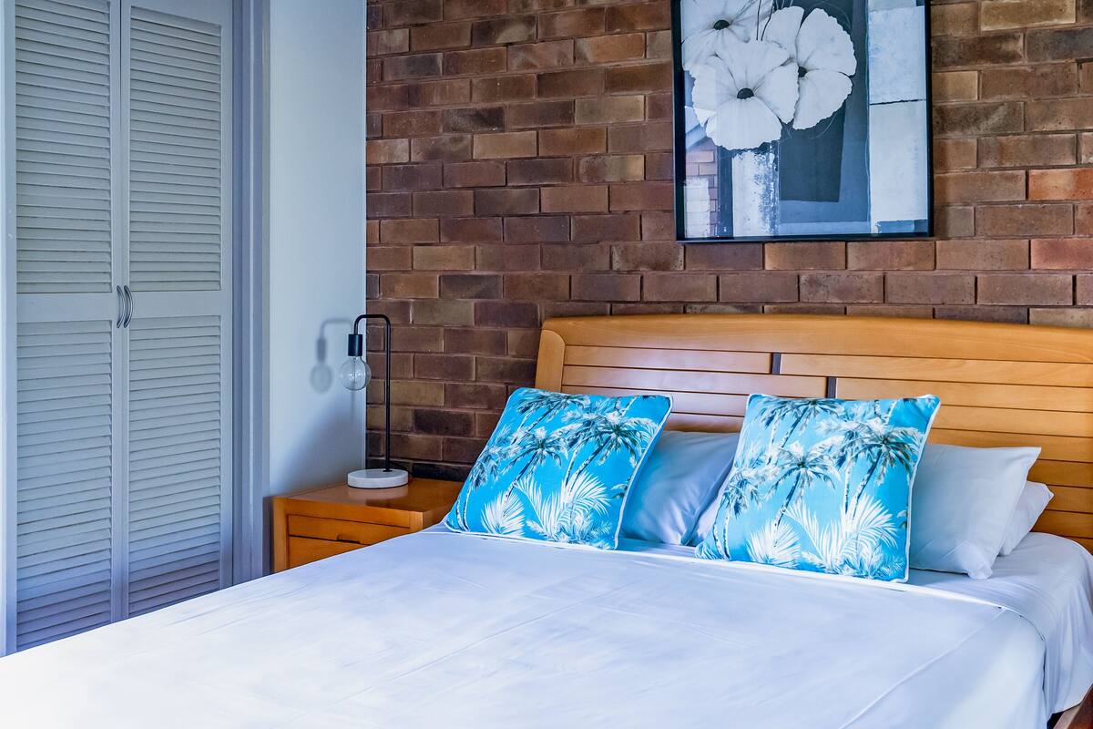 Ein Schlafzimmer mit Backsteinwand, Holz-Kopfteil und Bett mit weißer Bettwäsche.