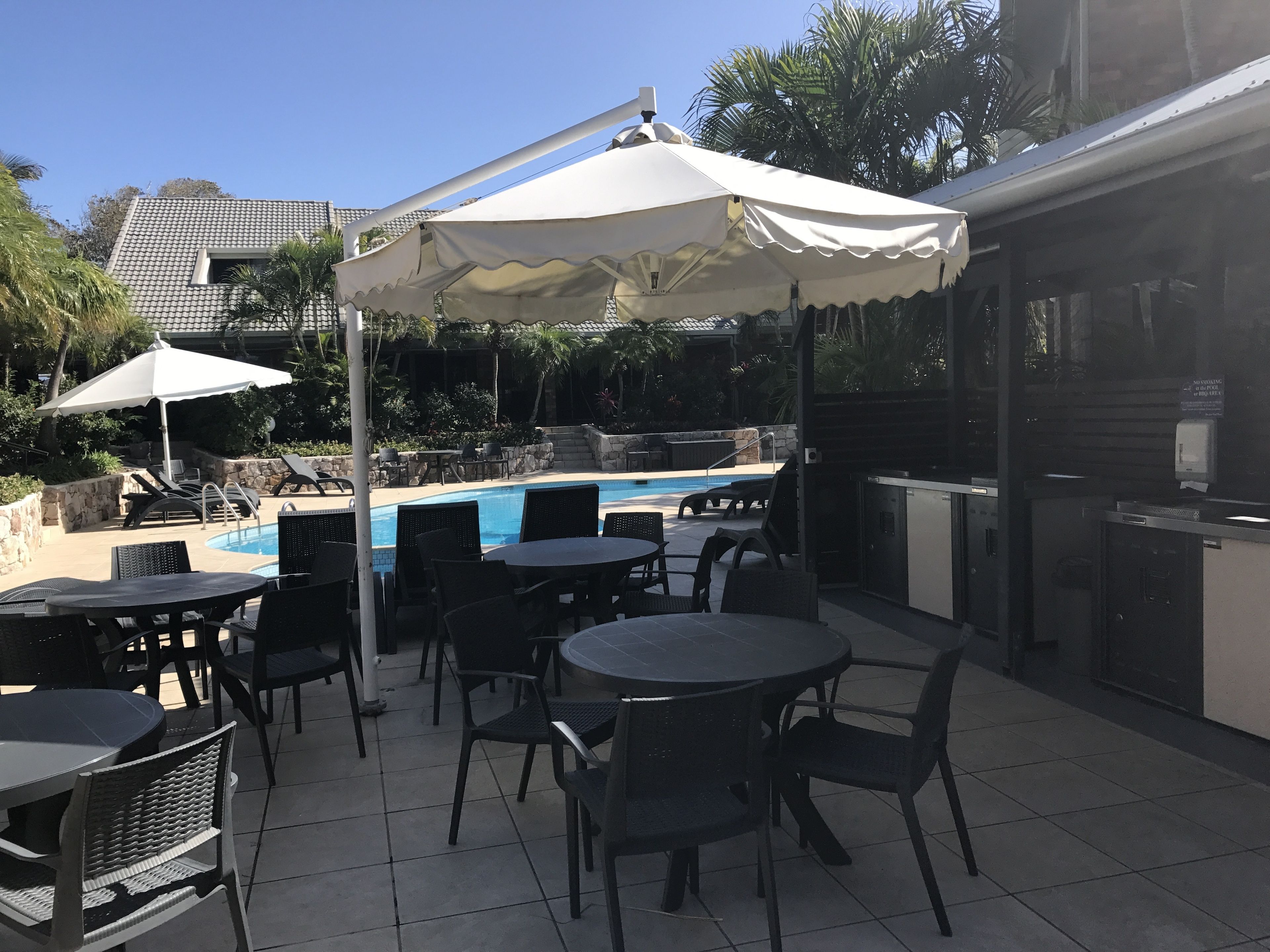 An outdoor pool area with lounge chairs and tables, a covered seating area, and a poolside bar.