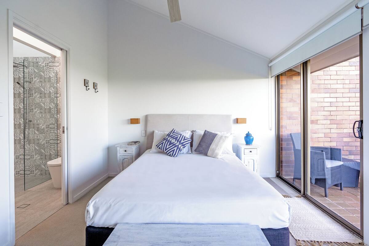 Ein Schlafzimmer mit einem großen Bett, einer Duschkabine aus Glas und Blick auf die Terrasse.