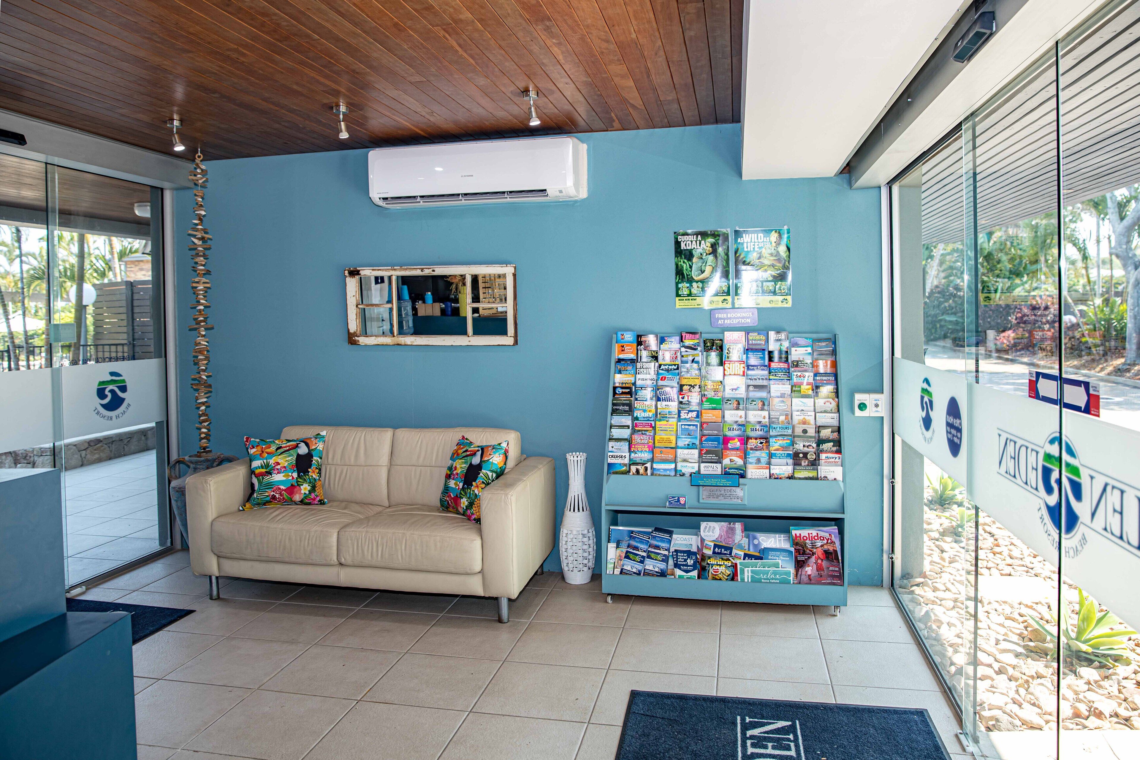 A reception area with a beige sofa, a magazine rack, and a blue wall.