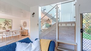 Uma sala de estar moderna com um sofá azul, uma escada de madeira e um espaço de jantar com cadeiras brancas e uma mesa de madeira.