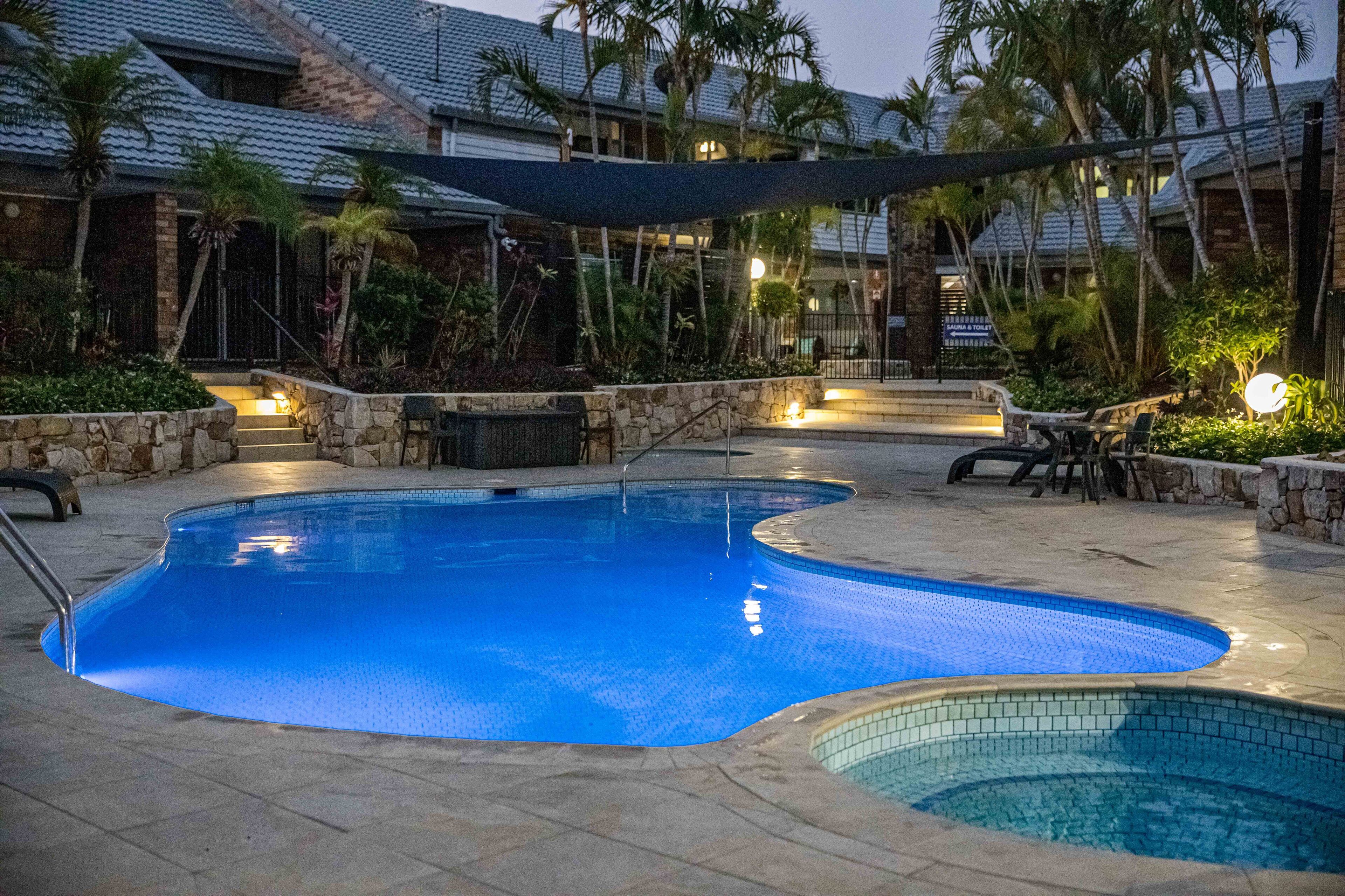 A swimming pool area with a stone border, a stone staircase leading to a building, and palm trees.