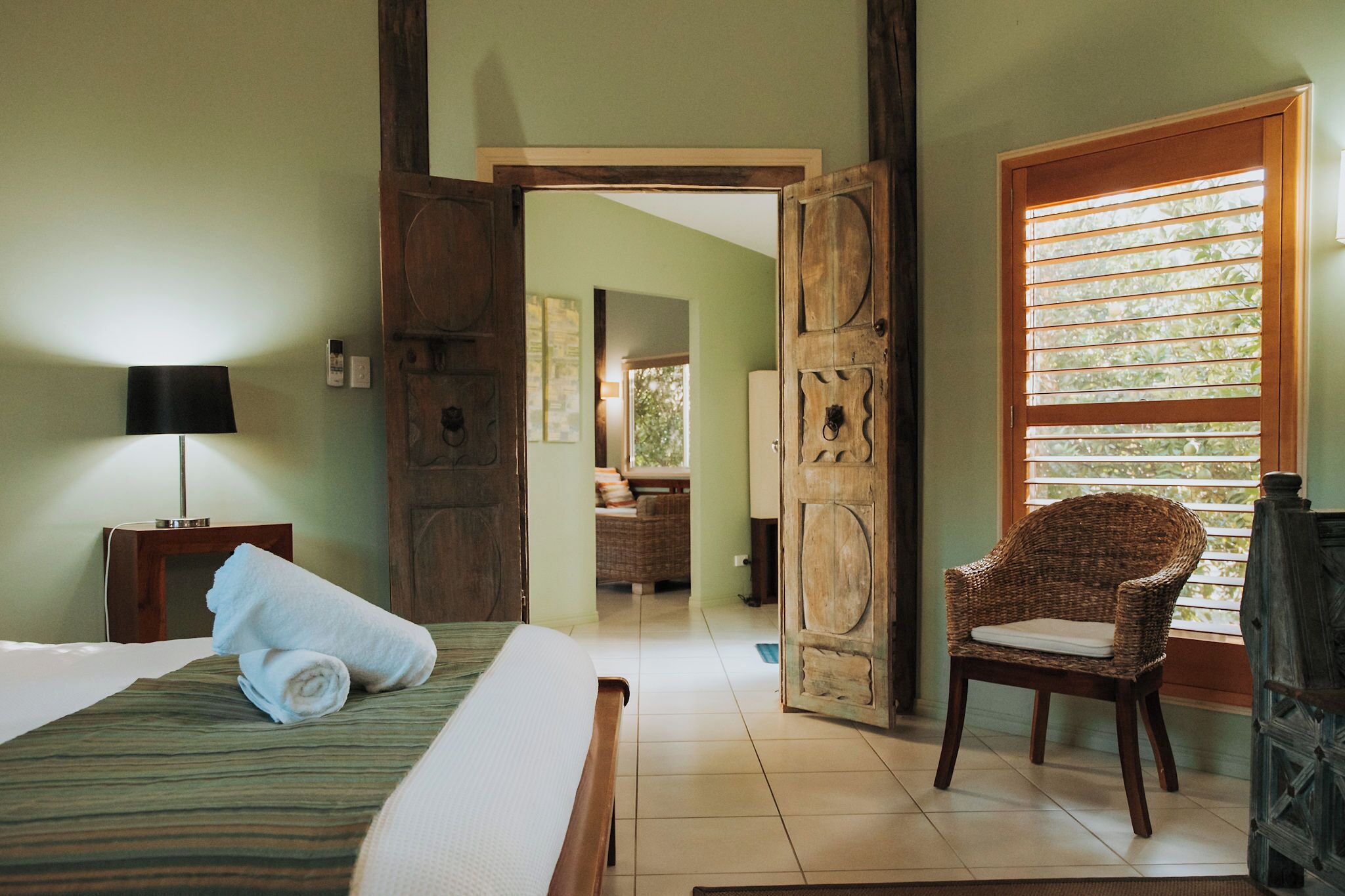 Une pièce avec un lit, une chaise, une lampe et une porte en bois.