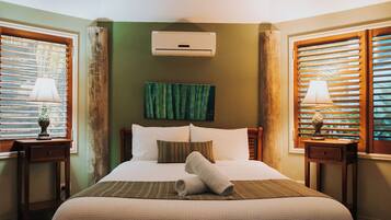 A hotel room with a bed, a wall-mounted air conditioner, a painting, and two nightstands with lamps.